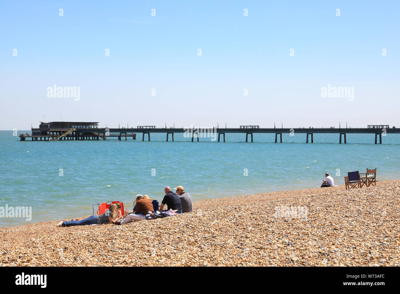 Sitzend auf dem Strand mit der historischen Seebrücke hinaus, in der Küstenstadt, an einem Sommertag, im East Kent, England, Großbritannien Stockfoto