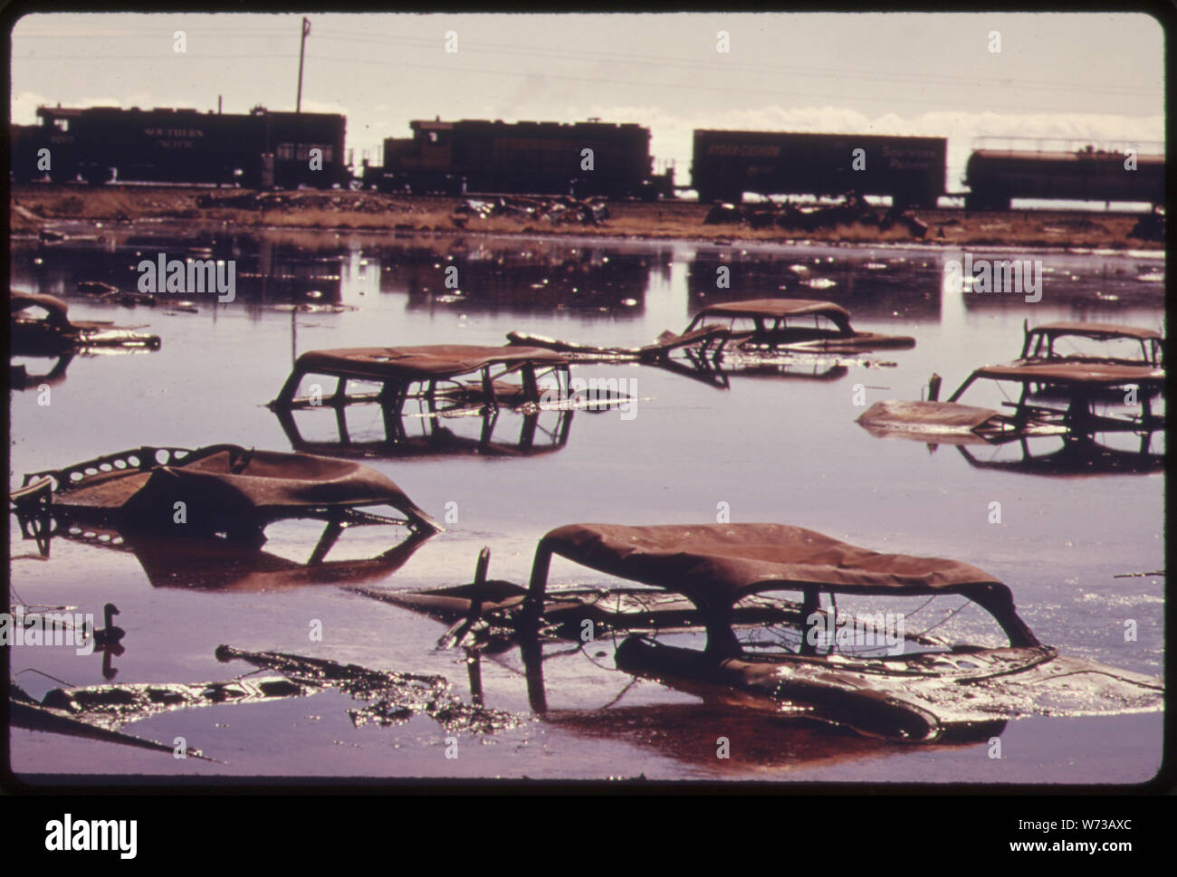 Zug auf der Southern Pacific Railroad an einem fünf Hektar großen Teich, DIENTE ALS DUMPAUFSTELLUNGSORT durch Bereich kommerzielle Unternehmen. Die Säure wasser-, öl-, säure- Ton, Schlamm, tote Tiere, AUSRANGIERTE AUTOS UND ANDERE DUMP ABLAGERUNGEN GEREINIGT WURDE VON MEHREREN STAATLICHEN GRUPPEN UNTER DER LEITUNG DES EPA. Einige 1.200.000 Liter Flüssigkeit wurde GEFÖRDERT VON DER WEBSITE, neutralisiert UND ZU EINEM ORT DER BESEITIGUNG Stockfoto