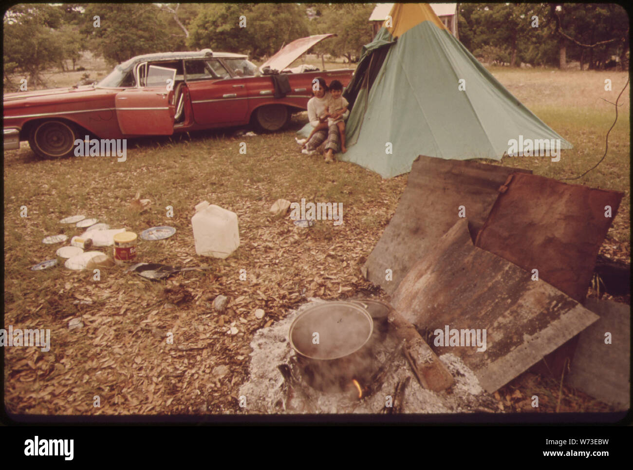 Frau und Kind von einem UMHERZIEHENDEN SCHAFEN 57309 WER ARBEITET FÜR EIN VIEHZÜCHTER IN DER LEAKEY, TEXAS UND SAN ANTONIO. Die Frau kocht ihr Essen auf dem offenen Feuer IM VORDERGRUND; die Familie lebt im Zelt aufgeschlagen neben ihrem Auto Stockfoto