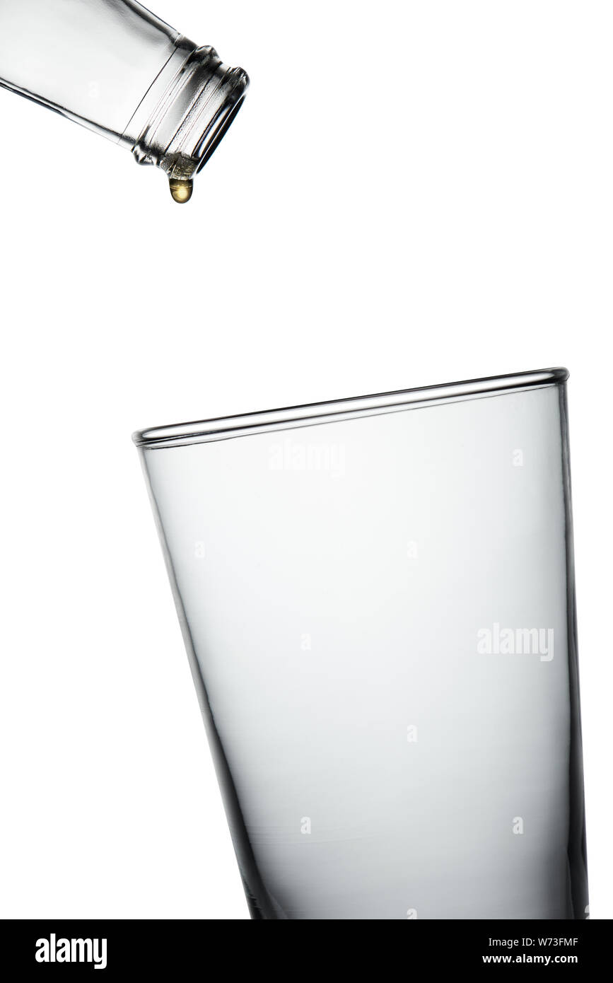 Leere Flasche mit letzten Tropfen trinken Tropfen in das leere Glas. Stoppen Sie die Nahaufnahme auf weißem Hintergrund. Stockfoto