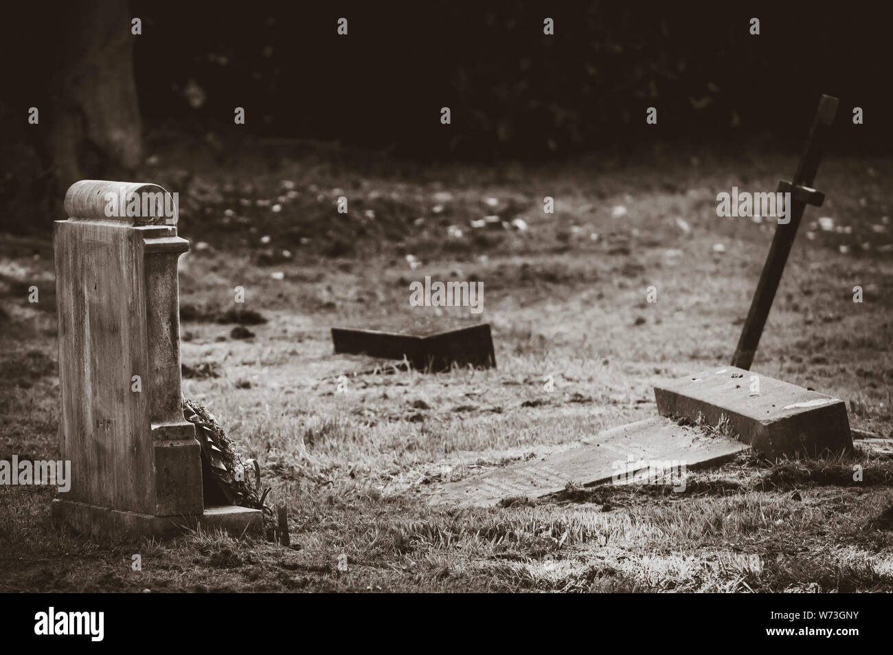Schwarz/Weiß-Bild eines gebrochenen Grabstein mit einem einzigen Kreuz hinter sich und ein Grabstein mit Kranz auf ihn vor. Stockfoto