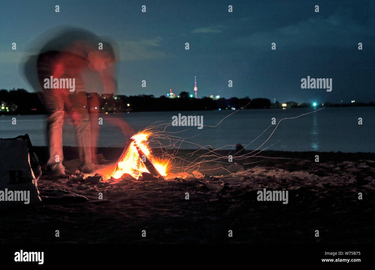 Nicht erkennbare Person mit unscharfen Motion, Strand, Lagerfeuer mit CN Tower in Toronto Skyline von Lake Ontario unter den Sternen am Himmel. Verschwommen m Stockfoto