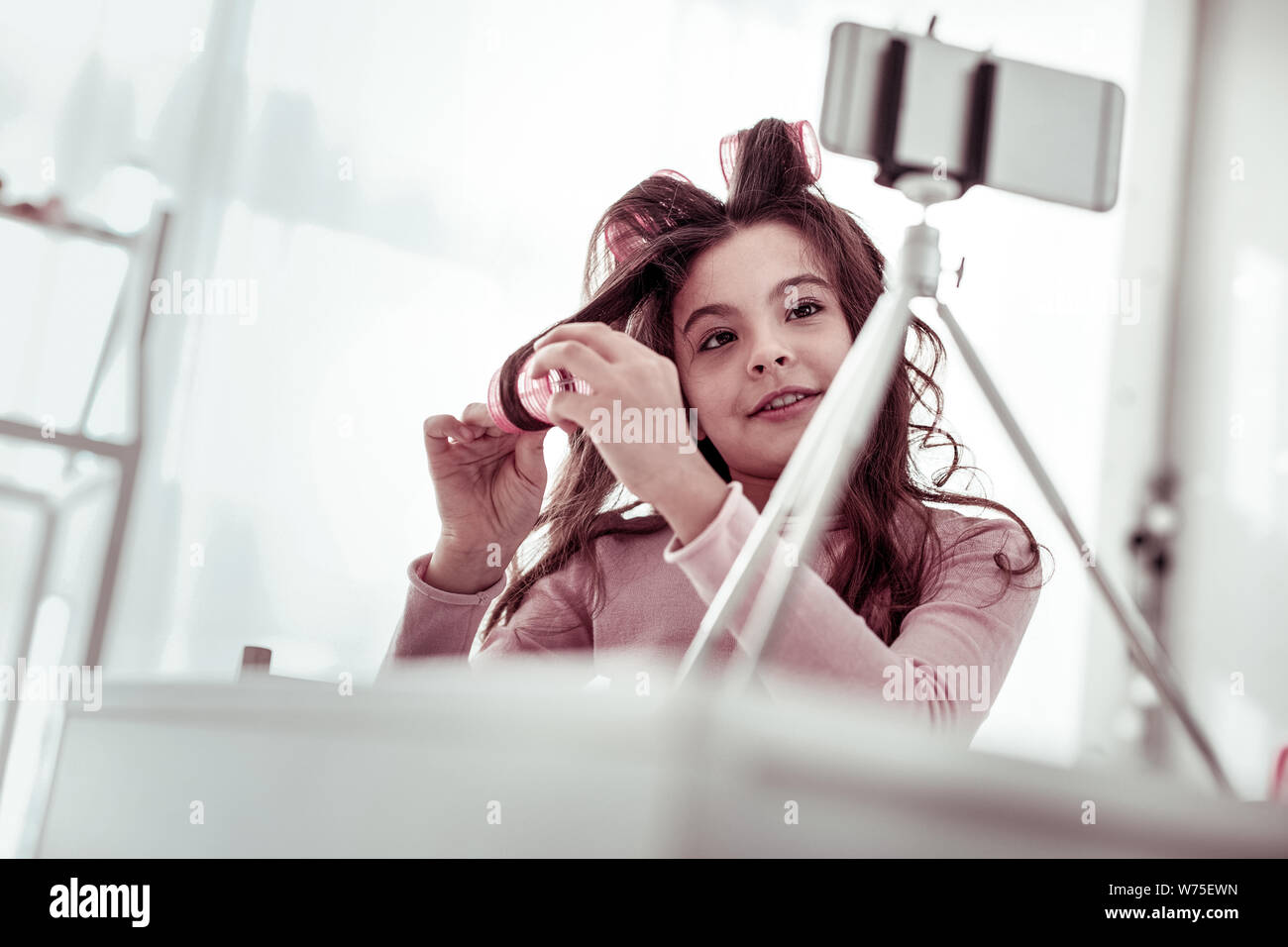 Schönes nettes Mädchen zeigen, wie Haar zu Rollen verwenden Stockfoto