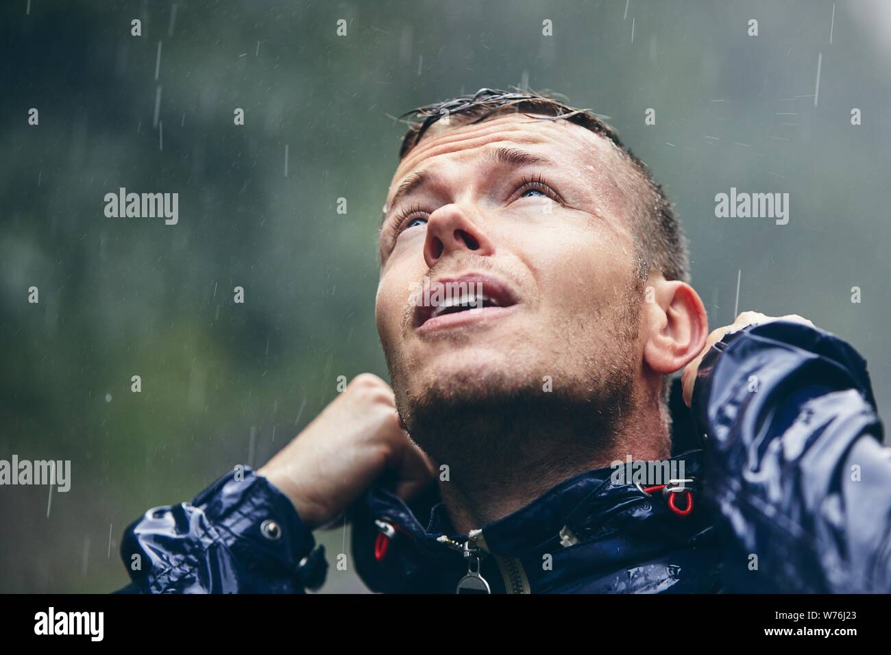 Reise bei schlechtem Wetter. Portrait des jungen Mannes in Durchnäßte Jacke im starken Regen. Stockfoto