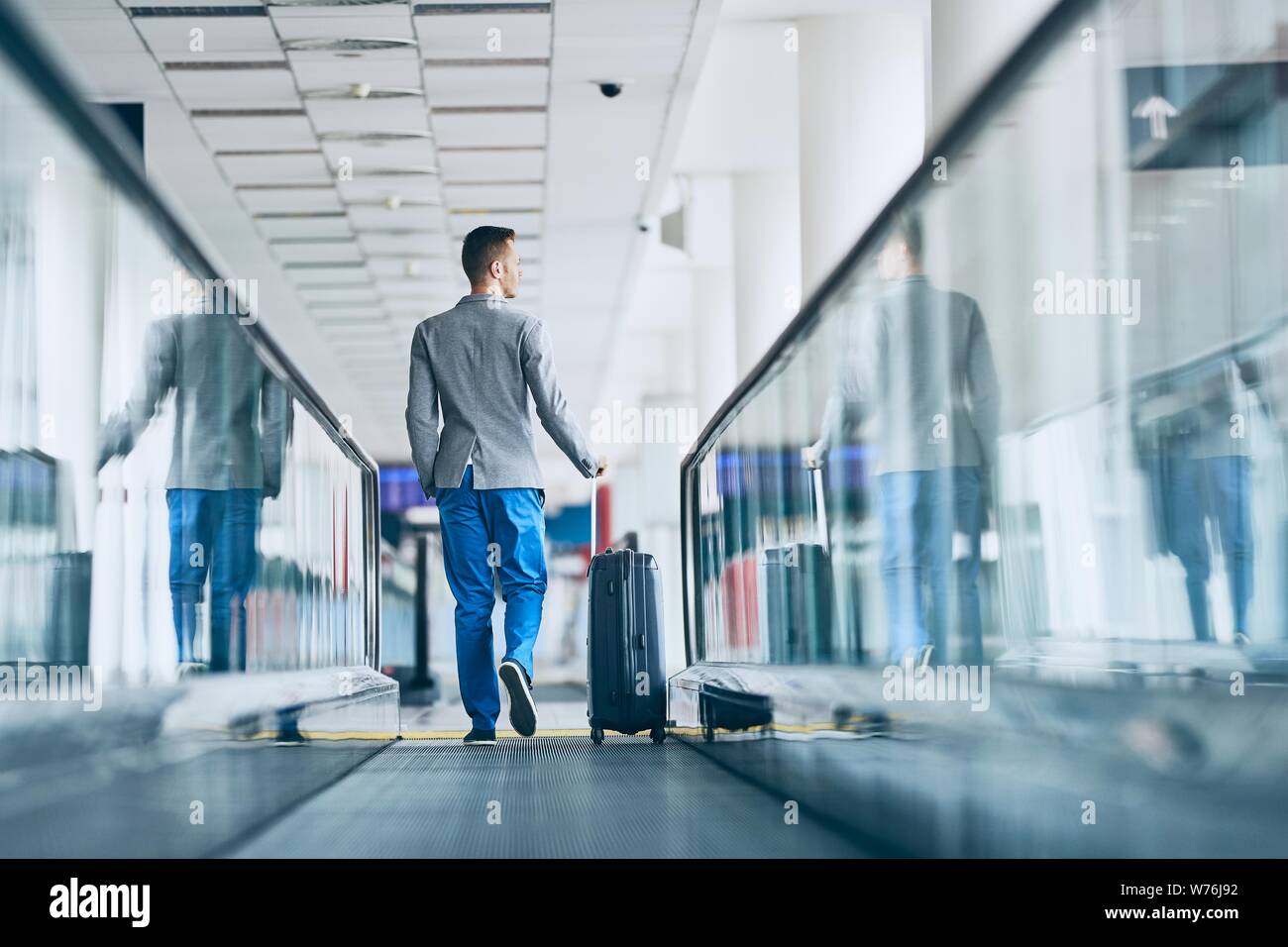 Gut gekleideter junger Mann mit dem Flugzeug. Geschäftsmann mit Gepäck zu Fuß auf travelator am Flughafen. Stockfoto