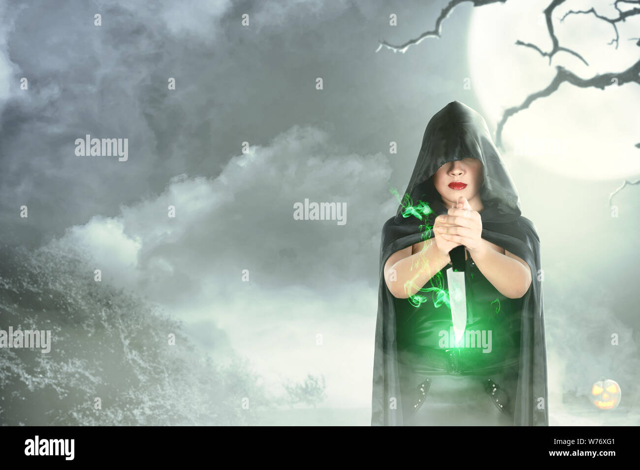 Hexe Frau in Schwarz mit Kapuze tun Ritual Magic mit einem Messer mit moonlight Hintergrund. Halloween Konzept Stockfoto