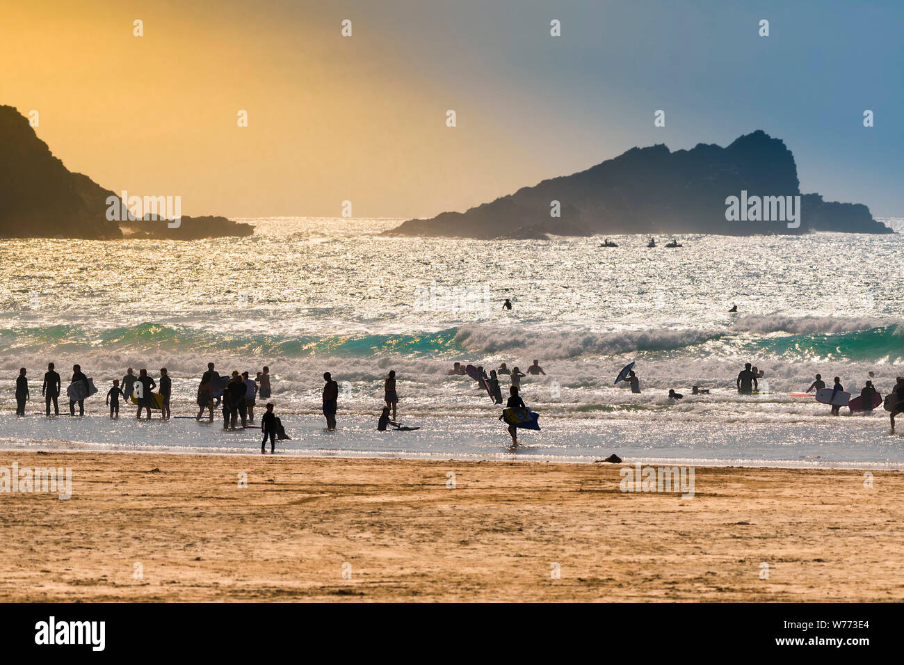 Urlauber silhouetted gegen die untergehende Sonne auf den Fistral Beach in Newquay in Cornwall. Stockfoto