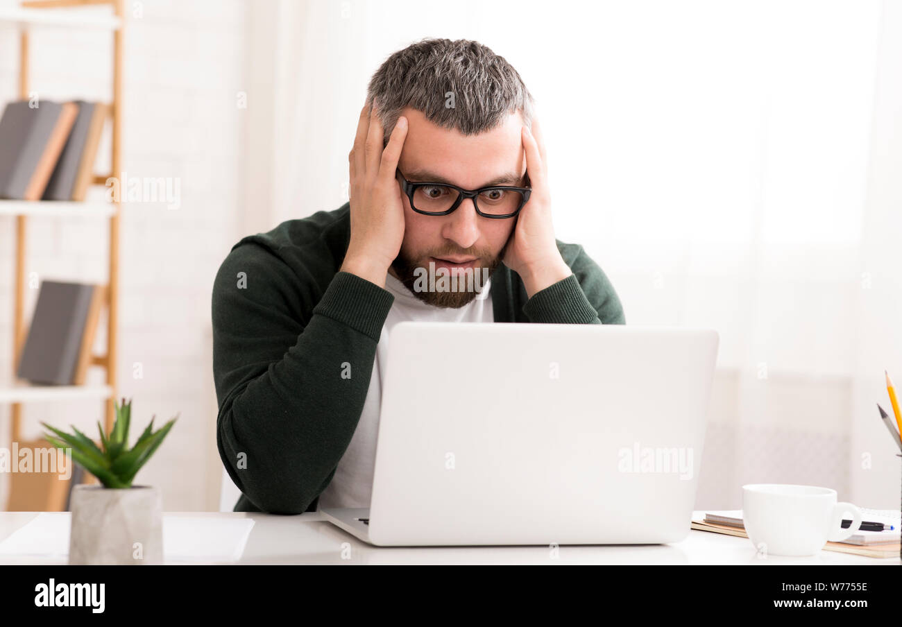 Schockiert kaukasischen Mann sitzt vor dem Laptop Stockfoto
