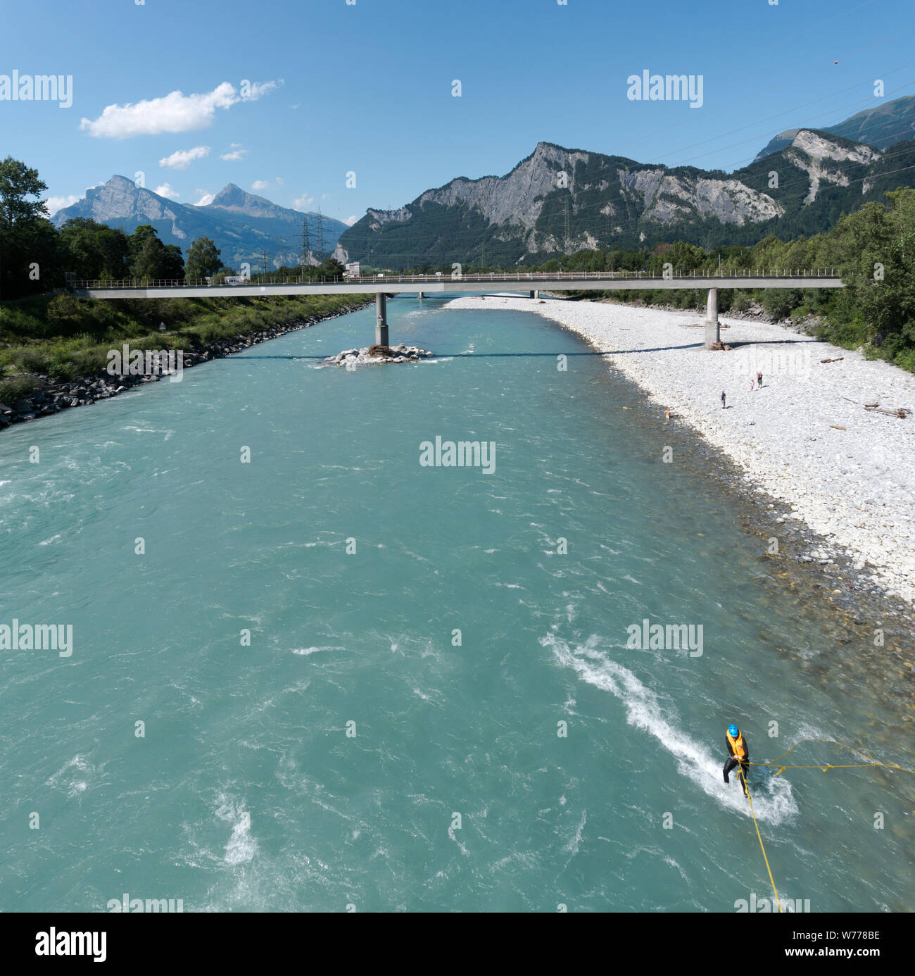 Maienfeld GR/Schweiz - 4. August 2019: Mann wakeboard Surfen auf einem Fluss mit einem Seil an einer Brücke und Berglandschaft hinter gebunden Stockfoto