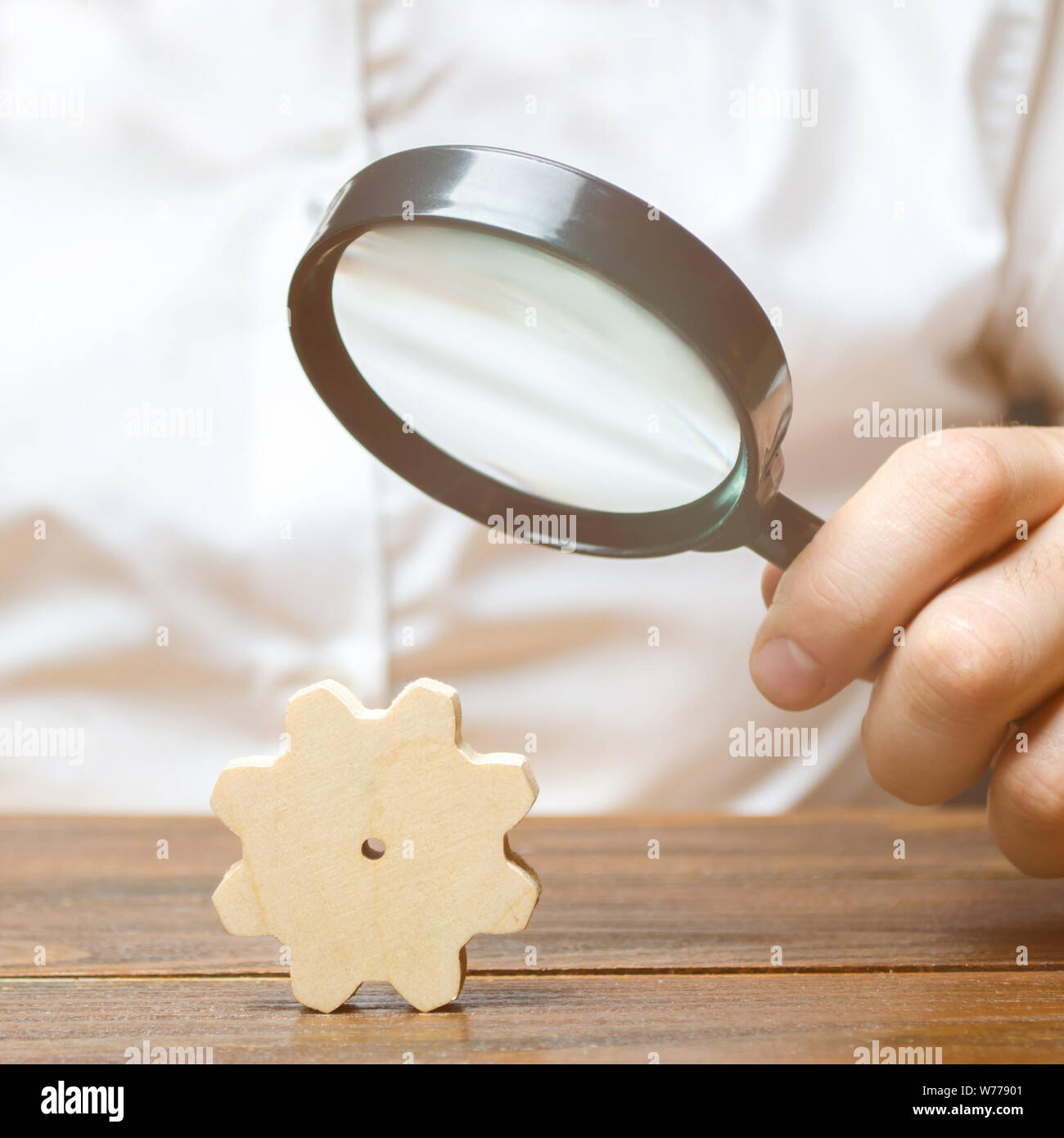 Geschäftsmann untersucht eine Holz- gang durch ein Vergrößerungsglas. Ein Rädchen in einer großen Maschine. Jede kleine Sache ist wichtig. Untersuchung und Analyse Stockfoto