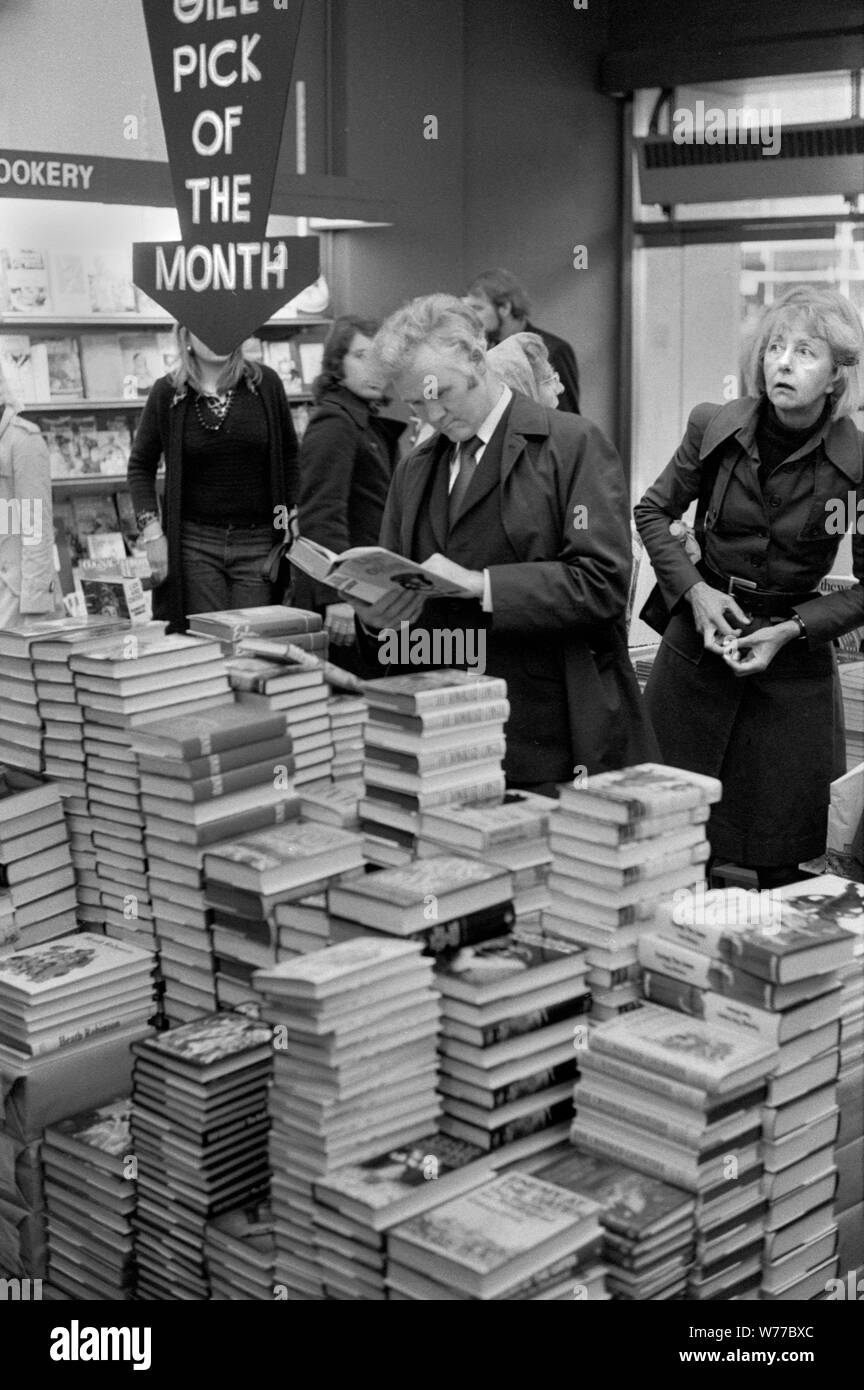 1970er beschäftigt überfüllten Buchladen Menschen Browsen, Einkaufen Kauf Entscheidung, welches Buch zu kaufen. Pick des Monats Stapel von Büchern. Hoch gestapelt. 70ER JAHRE UK HOMER SYKES Stockfoto