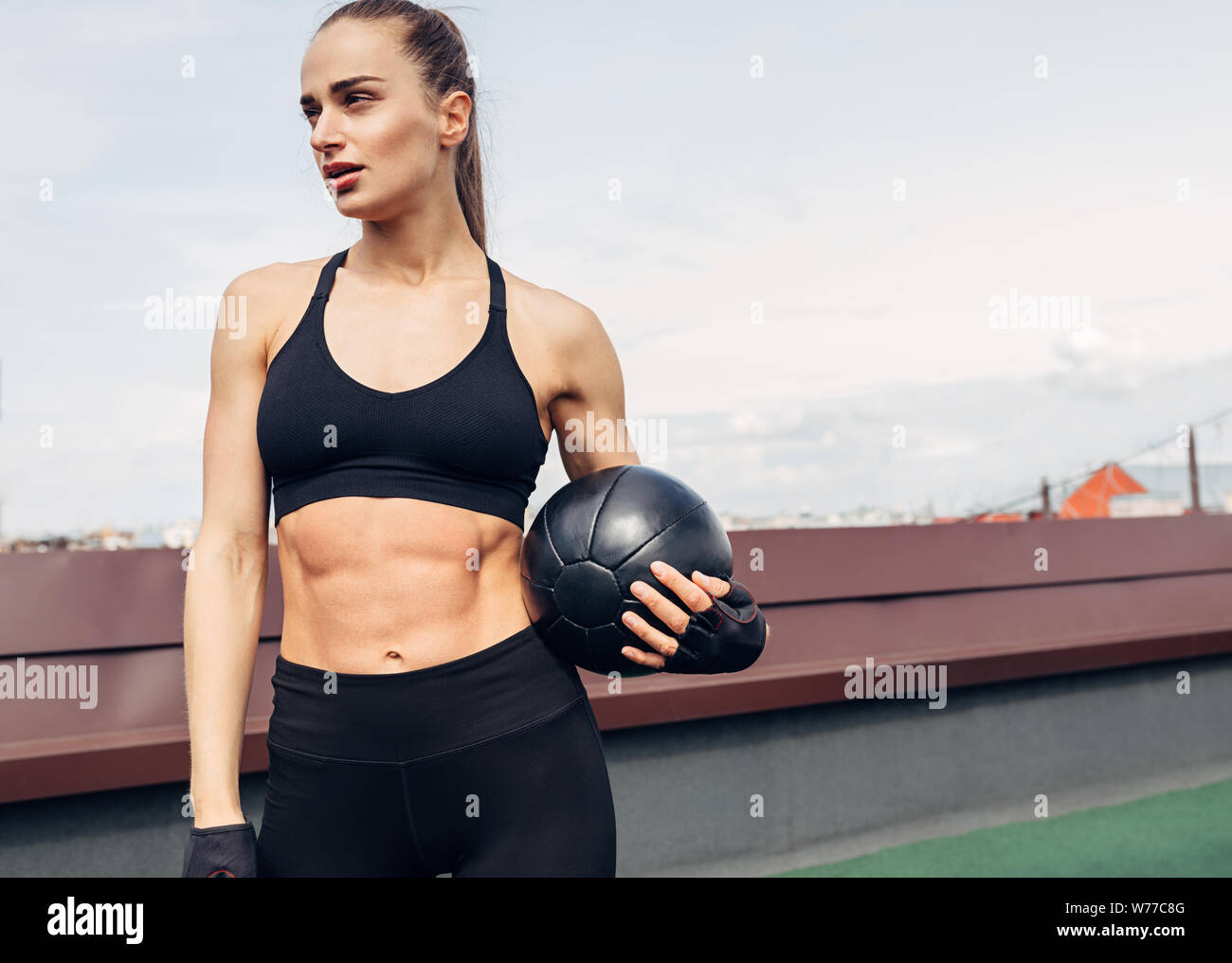 Frau in fitness Verschleiß stehen draußen auf einer Terrasse mit einem medizinball. Junge weibliche Ausruhen nach Training. Stockfoto