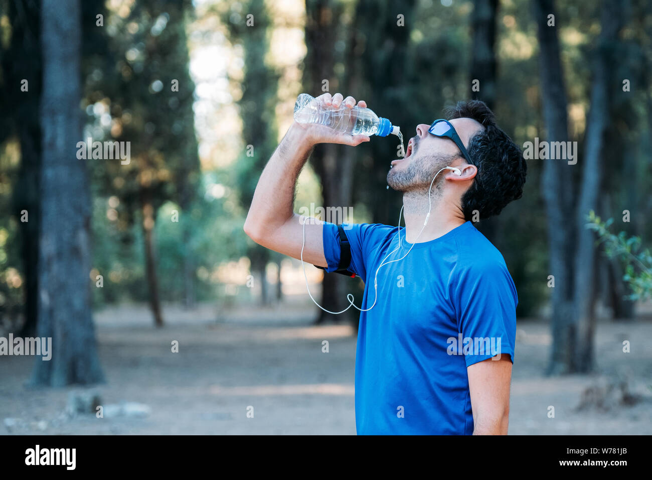 Weißer Mann Trinkwasser und das Hören von Musik in einem Park während des Trainings. Stockfoto