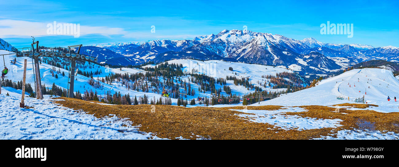 Atemberaubende Landschaft von Dachstein West Alpen, bedeckt mit Schnee und Pinienwäldern, mit Blick auf das Schnelle, Sesselbahn mit Sportlern, die zu Stockfoto