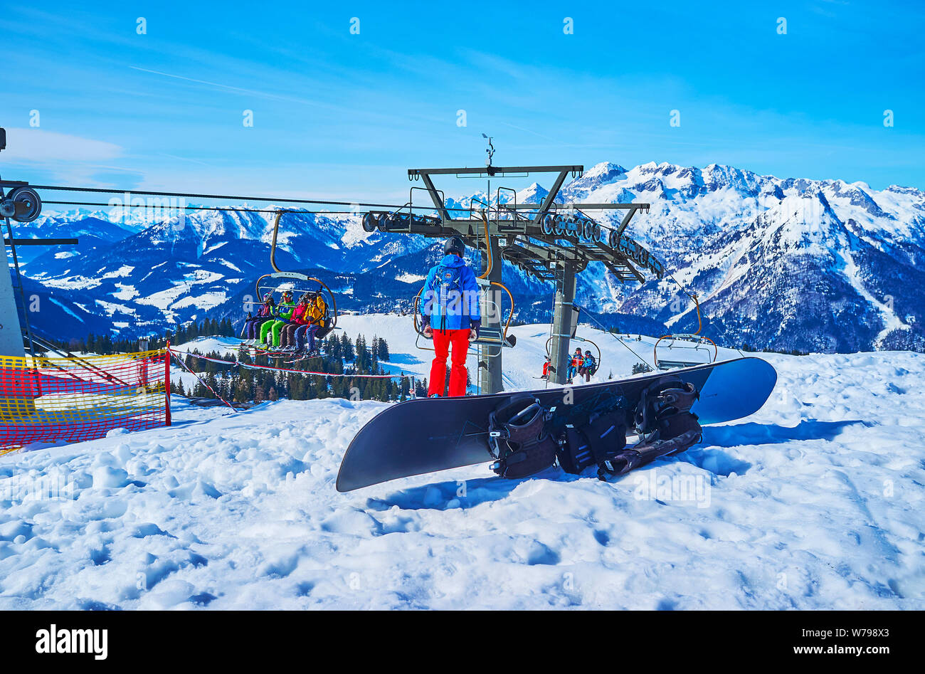 GOSAU, Österreich - 26. FEBRUAR 2019: Die chairliftfahrten über den schneebedeckten Hang der Zwieselalm Berg mit Blick auf das Snowboard im Vordergrund, auf Fe Stockfoto