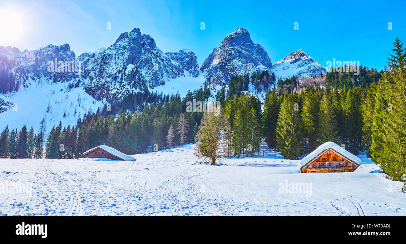 Die steilen schneebedeckten Hang mit Blick auf die kleinen Holzhäuser, hohen Bäumen und scharfen felsigen Gipfeln von Donnerkogl Berge von Dachstein West Bereich Fichte, Gos Stockfoto