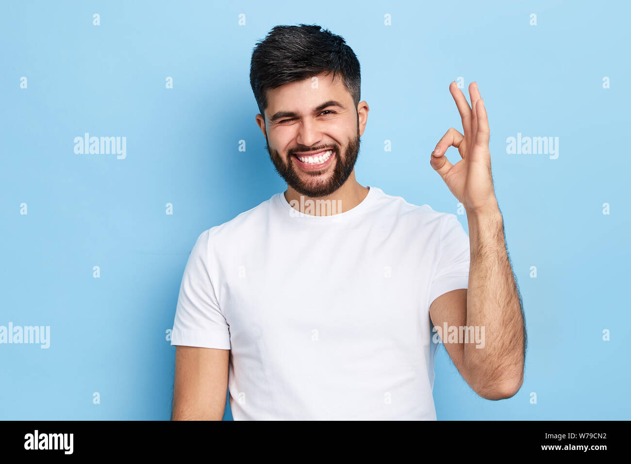 Gerne lustig, bärtiger Mann zwinkerte seinem Auge und zeigt ok Zeichen, auf blauem Hintergrund isoliert, alles unter Kontrolle ist. Witz, Spaß Konzept Stockfoto