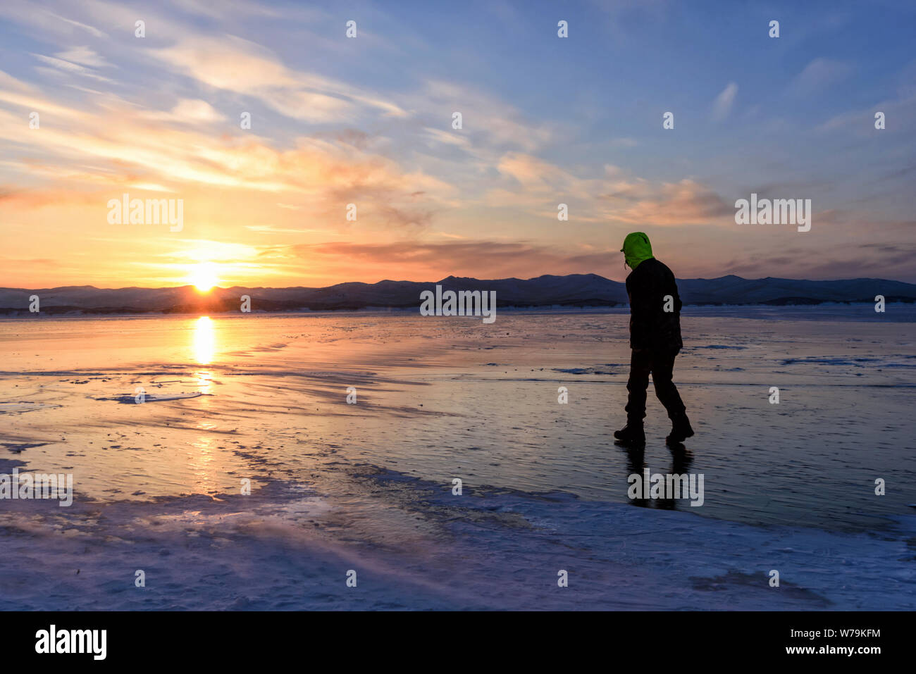 Silhouette eines Mannes, der auf dem Eisboden am baikalsee mit Sonnenuntergang läuft. Stockfoto
