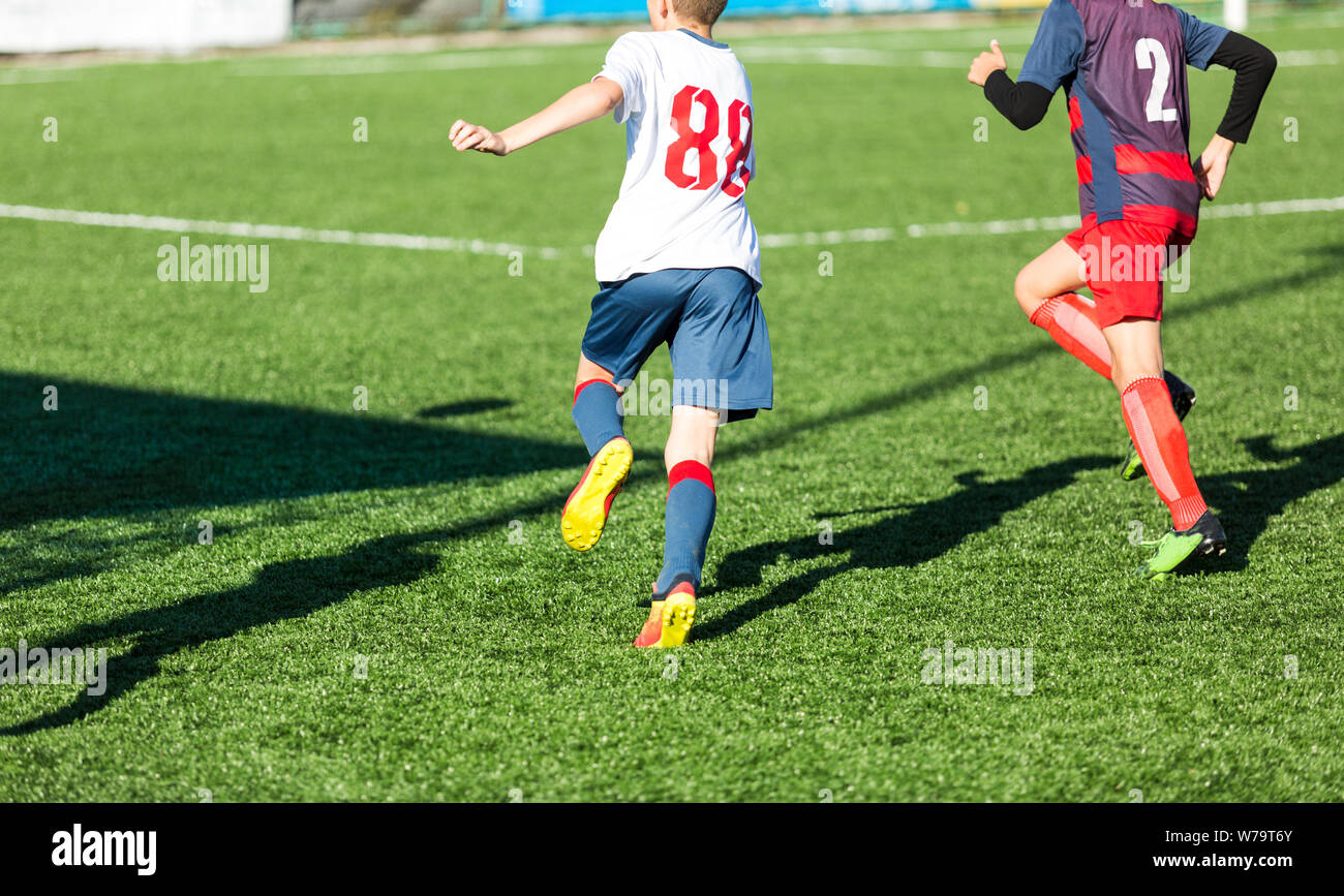 Jungs in Rot und Blau Sportswear spielt Fußball auf dem Feld, dribbelt Ball. Jungen Fußball-Spieler mit Ball auf grünem Gras. Training, Fußball Stockfoto