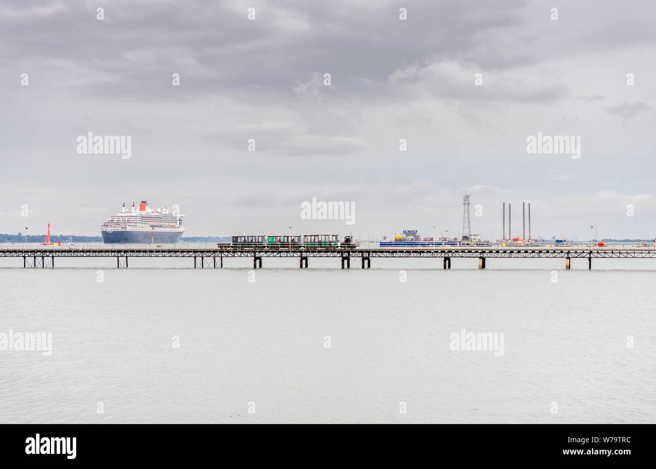 Hythe Pier an einem bewölkten Tag grau mit der "Queen Mary 2" verlässt den Hafen von Southampton, Hythe Waterfront, in der Nähe von Southampton, Hampshire, England, Großbritannien Stockfoto