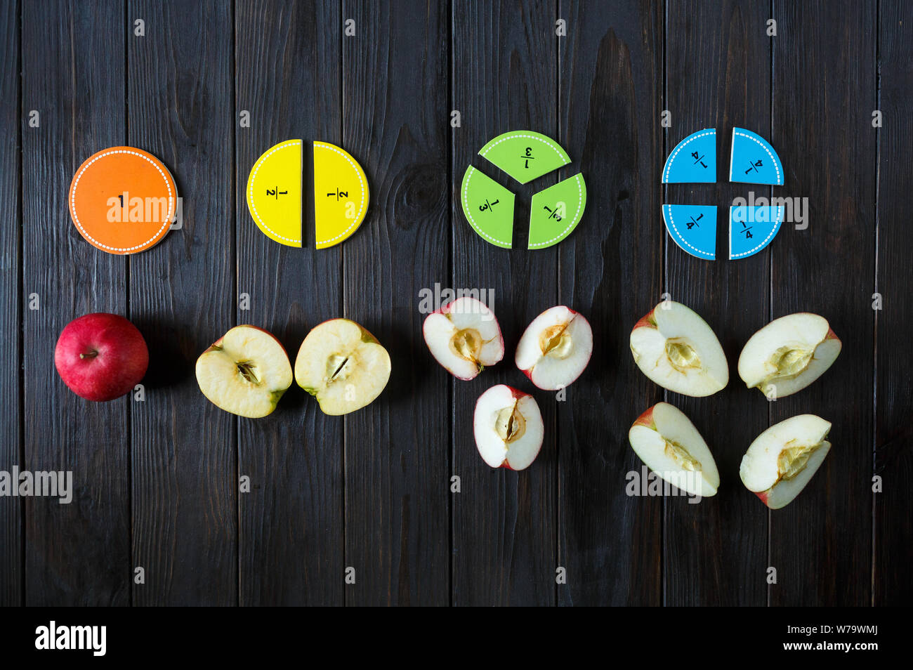 Bunte mathematische Fraktionen und Äpfel als Probe auf braunem Holz- Hintergrund oder Tisch. interessante Mathe für Kids. Bildung, zurück in die Schule. Stockfoto