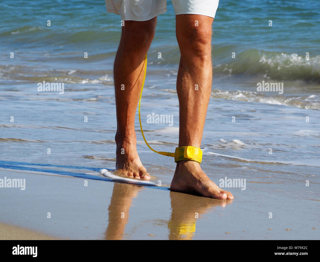 Close-up ein Surfer zu Fuß am Strand entlang auf seinem Fuß eine gelbe Leine. Atlantik. Sandstrand. In shorts gebräunte Beine angezogen. Stockfoto