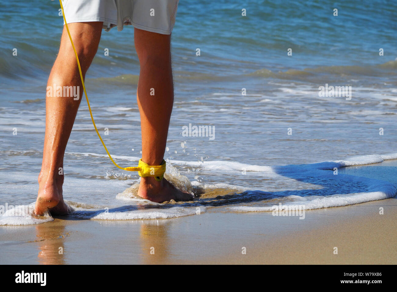 Close-up ein Surfer zu Fuß am Strand entlang auf seinem Fuß eine gelbe Leine. Atlantik. Sandstrand. In shorts gebräunte Beine angezogen. Stockfoto