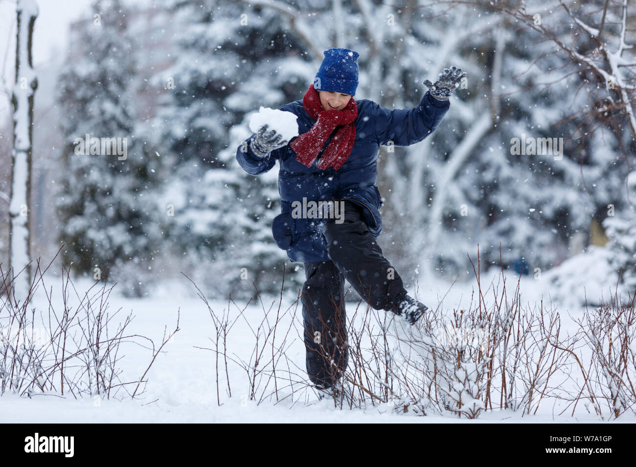 Kind springt und spielt Schneebälle im Winter Park Stockfoto