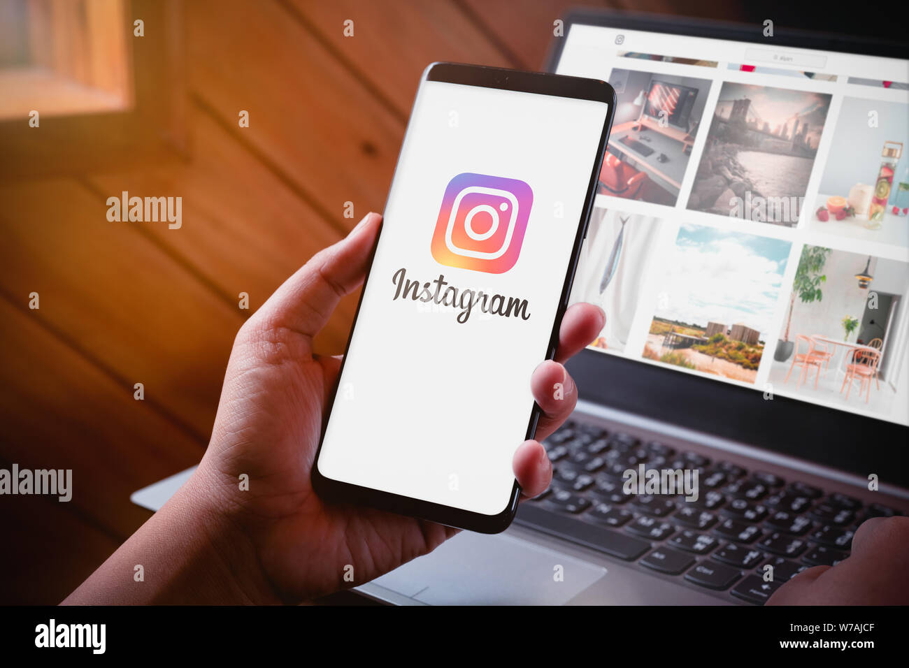 Bangkok, Thailand - August 6, 2019: Hände halten Smartphone mit Instragram Logo auf dem Bildschirm und Instragram website auf Laptop Hintergrund. Instagram ist La Stockfoto