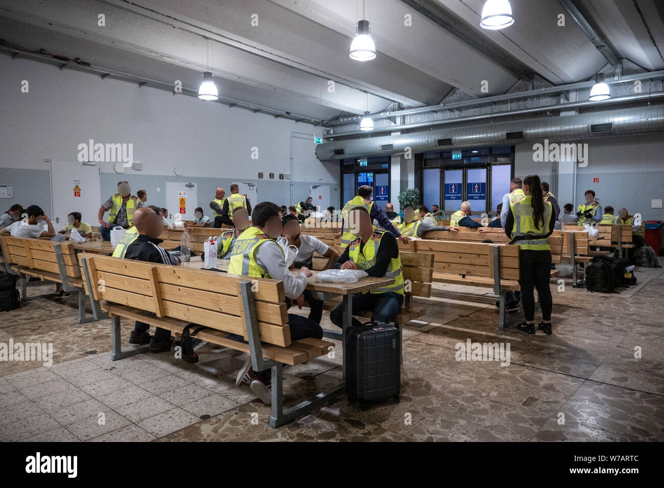 01. August 2019, Sachsen, Leipzig: Polizisten warten mit Afghanen am Flughafen Leipzig-Halle in der Abflughalle. In der Halle, Tische und Bänke waren besonders solide, um mögliche Ausschreitungen zu vermeiden. 45 abgelehnte Asylbewerber auf der Flucht in die afghanische Hauptstadt Kabul deportiert wurden. (Achtung: die Gesichter der zivilen Polizisten wurden unkenntlich auf Antrag des Ministeriums des Innern, die Gesichter der Deportierten unkenntlich sind aus Gründen der Persönlichkeit Schutz; über dpa-Geschichte: Abschiebung Flug nach Afghanistan) Foto: Michael Kappeler/dpa Stockfoto