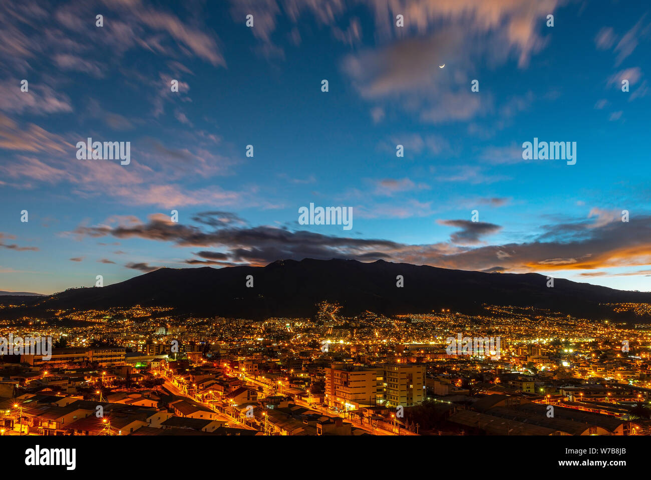 Lange Belichtung Stadtbild von Quito bei Nacht mit einem Halbmond und der eindrucksvollen aktiven Vulkan Pichincha, Ecuador. Stockfoto
