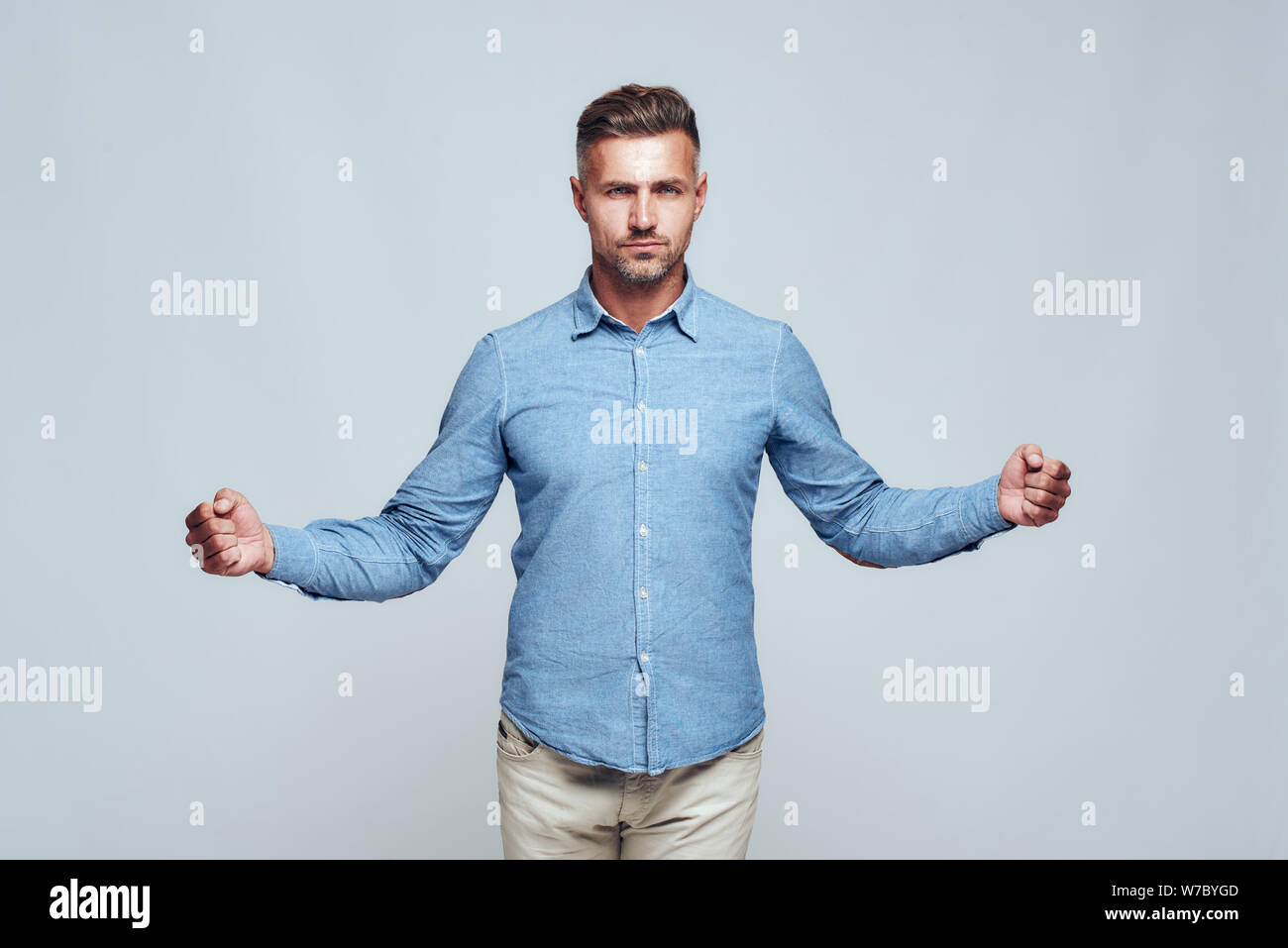 Ich bin stark. Selbstbewusster und gutaussehender bärtiger Mann in legerer Kleidung, der die Hände in Fäusten zusammenhält, während er vor grauem Hintergrund steht. Stärke und Motivation. Studioaufnahme Stockfoto