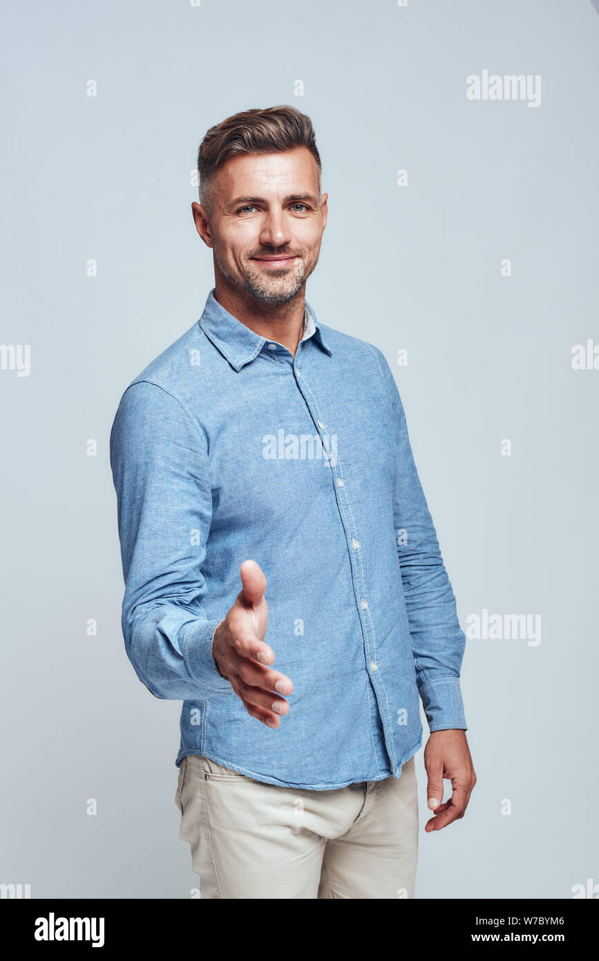 Hello Handsome lächelnden Mann in legerer Kleidung ist die Hand zu schütteln, während vor grauem Hintergrund stehen. Studioaufnahme. Positives Konzept. Besprechung Stockfoto