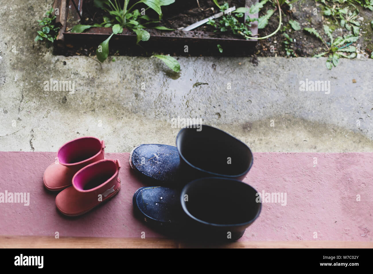 Zwei Gummistiefel Paare (Vater und Tochter) auf der Veranda am Eingang des Hauses während eines regnerischen Tag Stockfoto