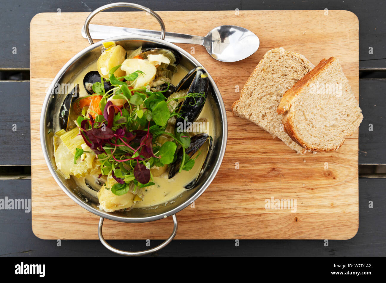 Eine Schüssel mit Seafood Chowder ist auf einem Holzbrett mit Brot serviert. Der Teller mit Kartoffeln und Salat. Stockfoto