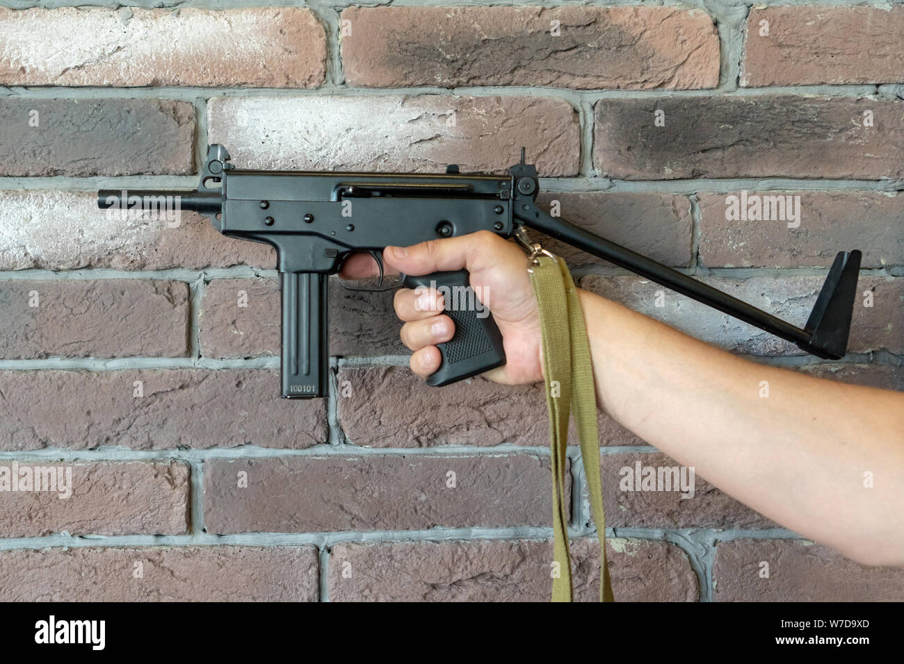 PP-91 Kedr Maschinenpistole. Ein Mann hält ein Maschinengewehr in der Hand auf dem Hintergrund einer braunen Wand. Stockfoto
