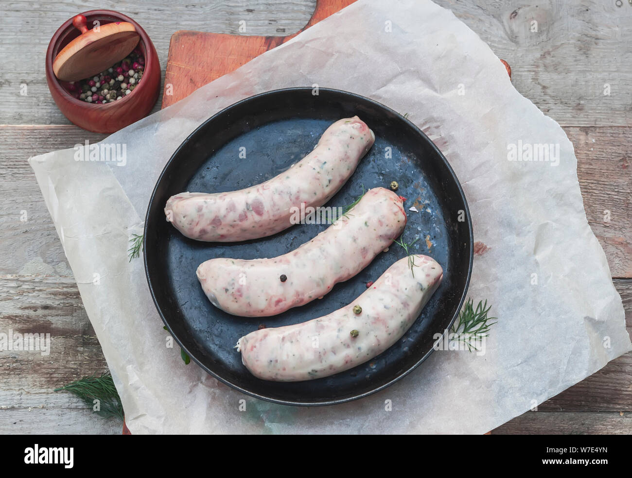 Frische Würste mit Gruenen und Gewürze für ein Barbecue auf einem eisernen Grillpfanne für das Kochen am Feuer Stockfoto