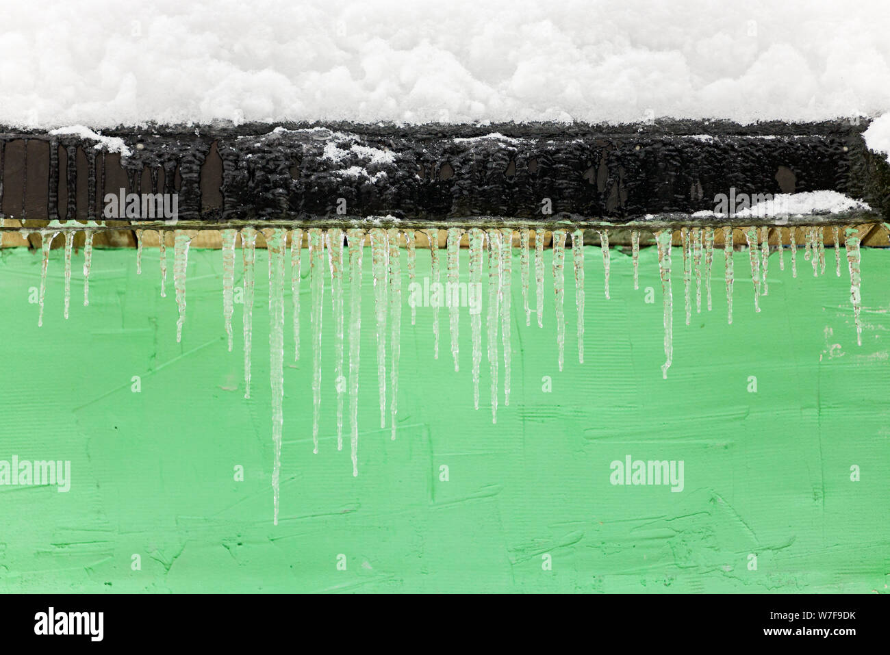 Eine Menge an gefrorenen Eiszapfen vor dem Hintergrund einer grünen Wand. frostige Wetter Stockfoto