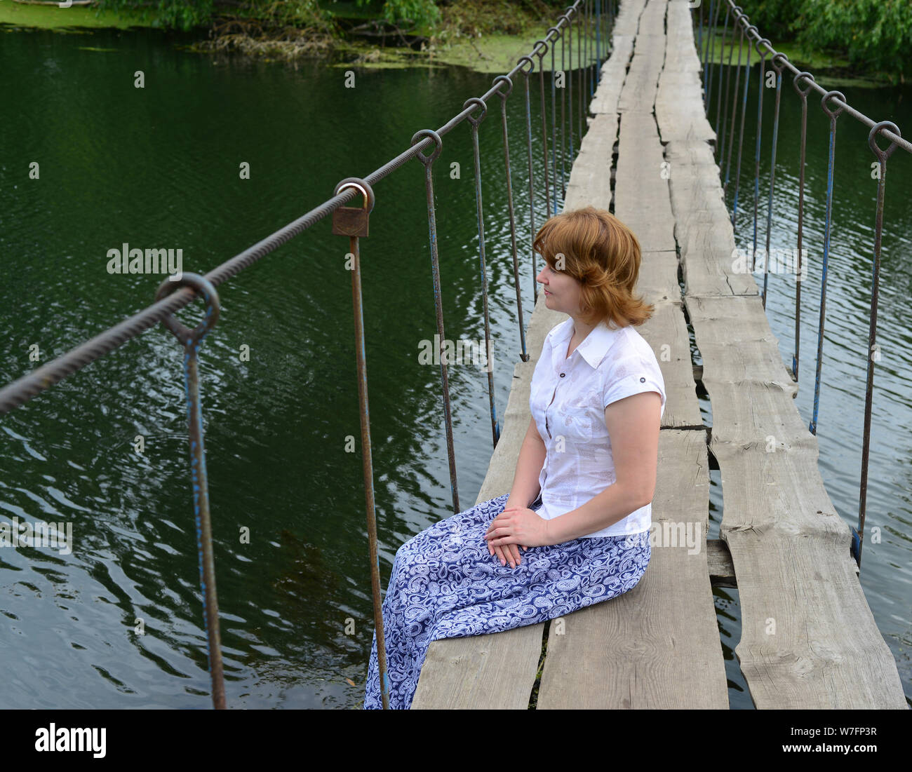 Frau sitzt auf einer Holzbrücke über den Fluss Stockfoto