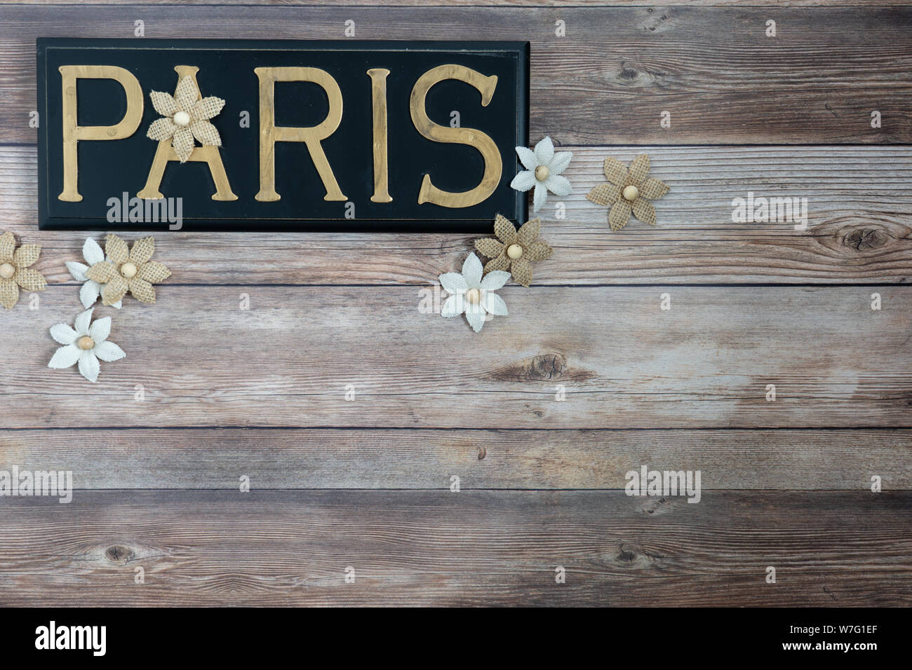 Paris Wort in Messing Buchstaben auf schwarz lackiertem Holz mit sackleinen Blumen auf eine gealterte Holzstäbchen Hintergrund Stockfoto