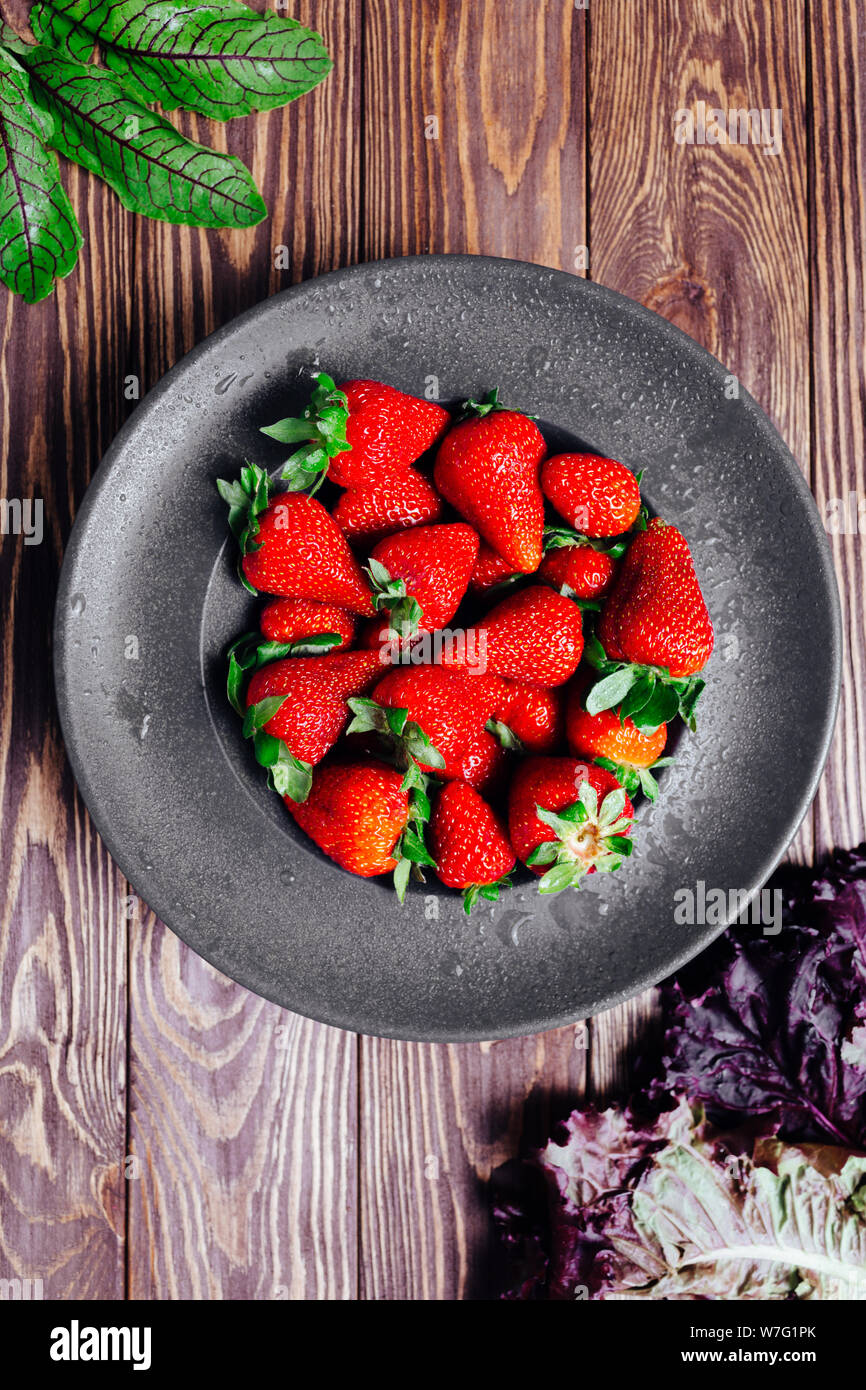 Erdbeeren in eine schwarze Platte auf einer hölzernen eco Hintergrund mit grünen. Stockfoto