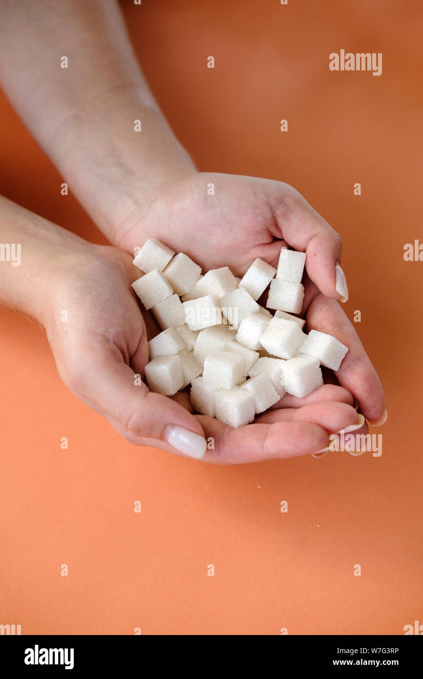 Woman Holding in den Händen weißer Zucker Würfel auf orangem Hintergrund. Diabetes, Zucker Krankheit, ungesundes Essen, Diät Konzept. Platz kopieren Stockfoto