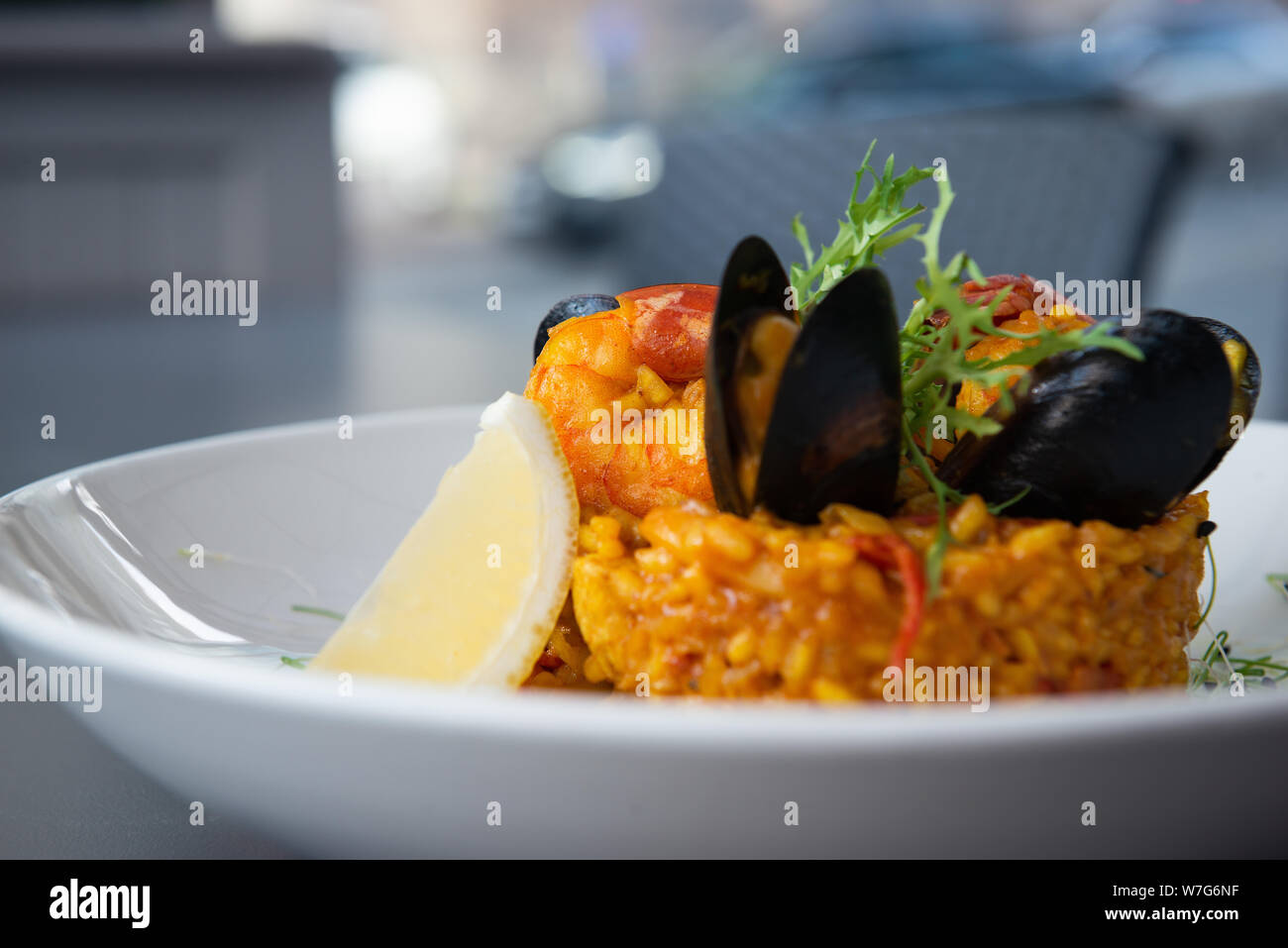 Spanische Paella mit Muscheln und Garnelen mit Zitrone und Rucola. Auf einem weißen Teller serviert. Nahaufnahme mit Bokeh. Main Reisgericht. Restaurant. Stockfoto