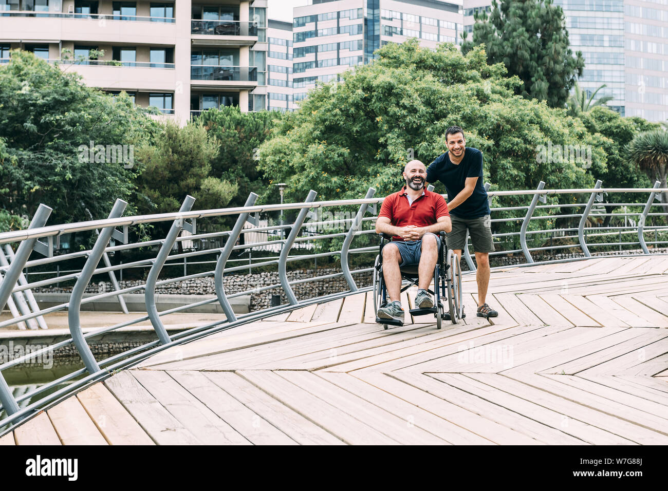 Behinderte Menschen im Rollstuhl wandern und Lachen im Park mit einem Freund, den Begriff der Freundschaft und der Integration von Menschen mit Behinderungen und Reduzierung Stockfoto