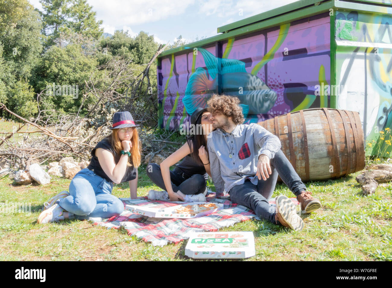 Gruppe von jungen multiethnischen bei einem Picknick im Grünen Pizza zu essen, die aufgeregt, indische Frau küsst die junge italienische Mann vor der Fren Stockfoto