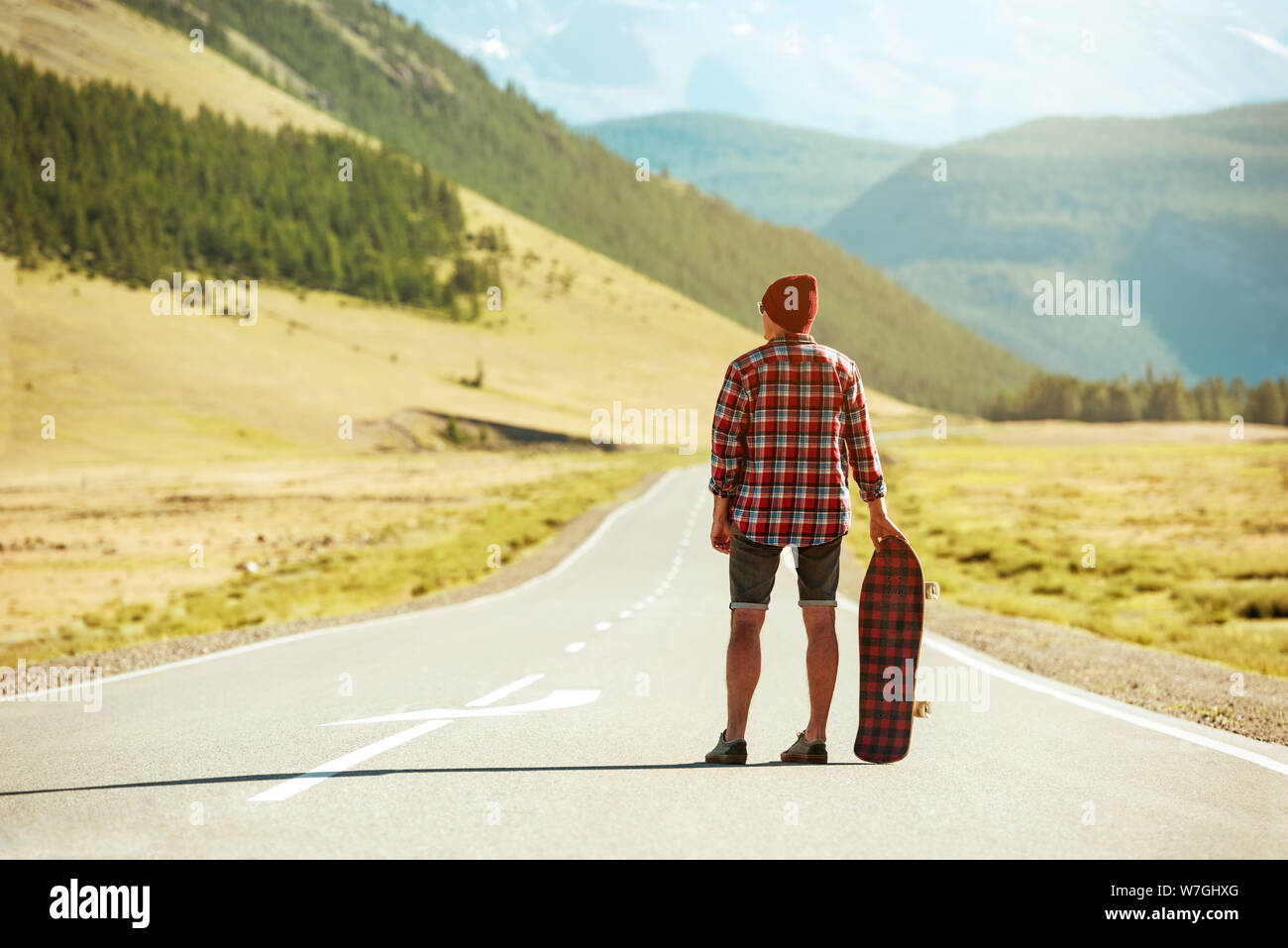 Hipster mit Longboard oder Skate steht auf langen geraden Straße in den Bergen Stockfoto