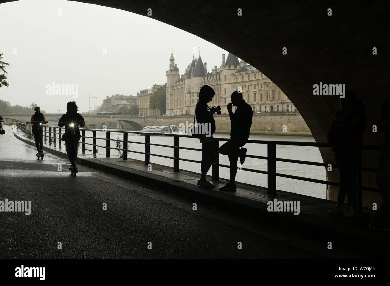 Unter der Brücke an der Seine an einem regnerischen Sommertag in Paris Frankreich. Ein Mädchen ihre Fotos auf Ihrer Kamera als drei Elektroroller vorbei. Stockfoto