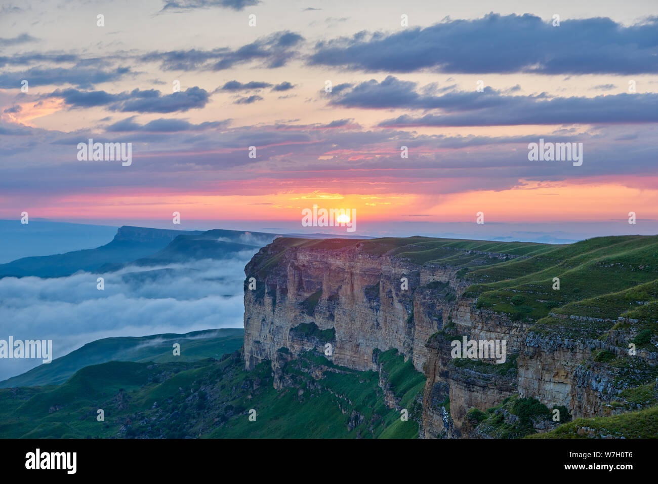 Sonnenuntergang in den Bergen. Die untergehende Sonne beleuchtet die Bergkette, Nebel und Wolken. Stockfoto