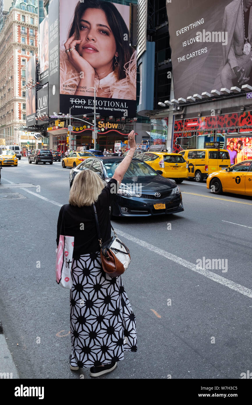 Eine Frau steht auf der Straße ein Taxi Hagel auf einer belebten Straße in Times Square, Midtown, New York Stockfoto