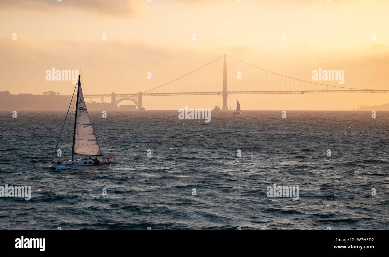 Die Golden Gate Bridge in San Fransisco, Kalifornien bei Sonnenuntergang mit einer kleinen Yacht segeln Vergangenheit Stockfoto